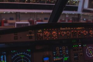 View from an airplane cockpit looking out onto an airport at night. Illuminated control panels add a dramatic feel.