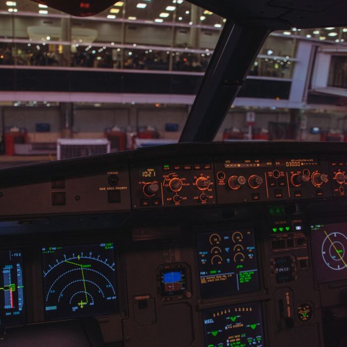 View from an airplane cockpit looking out onto an airport at night. Illuminated control panels add a dramatic feel.