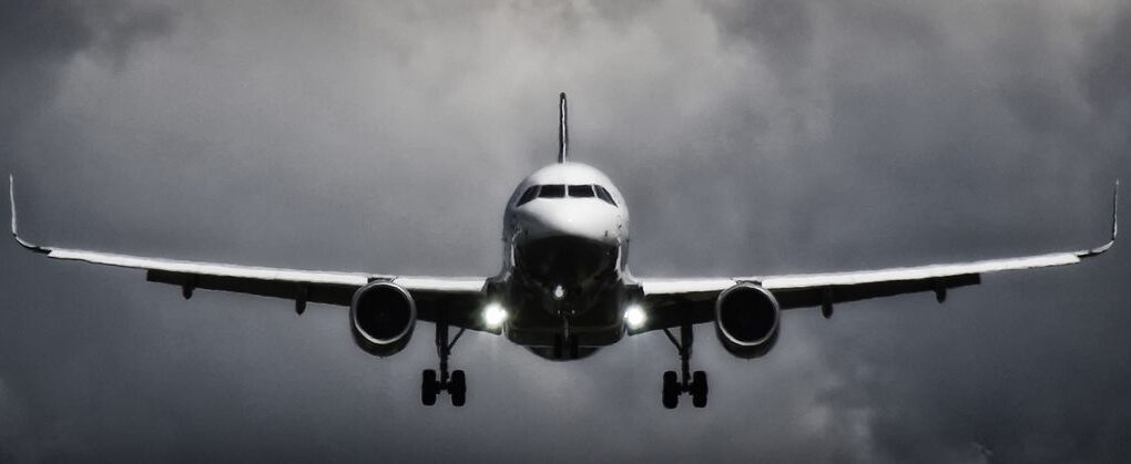 A dramatic view of an airplane landing with stormy clouds overhead, showcasing aviation in a monochrome scene.